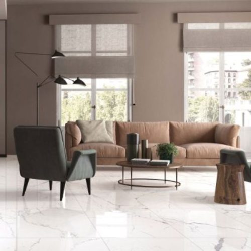 Modern living room featuring polished marble wall and floor tiles, cozy sofa, stylish armchair, and bright natural lighting.